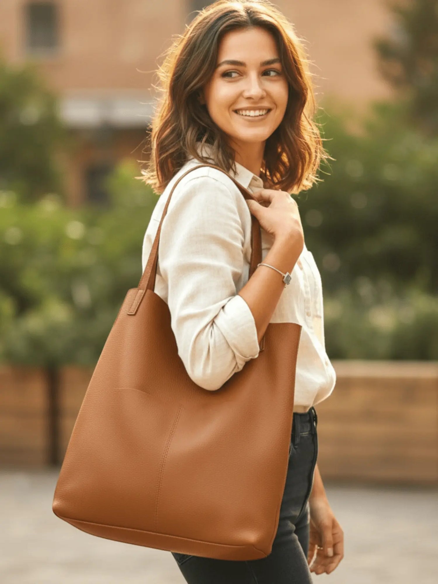 Femme souriante tenant un sac fourre-tout camel en cuir avec anse souple