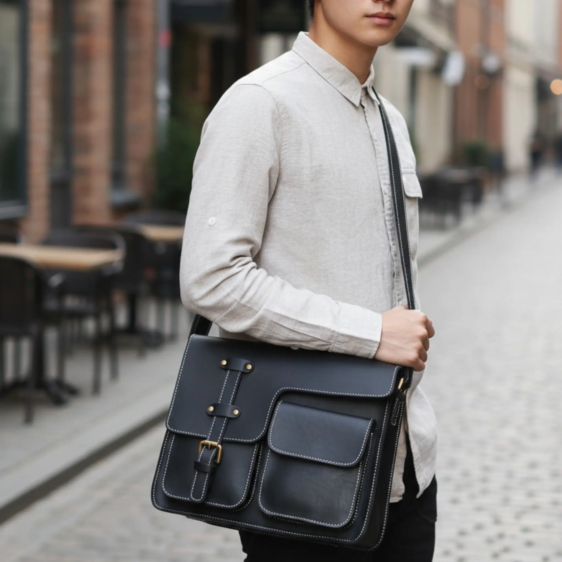 Homme portant un cartable en cuir noir en bandoulière, style professionnel et moderne.