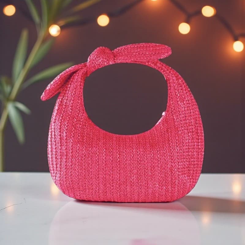 Pochette bohème en paille rose avec nœud, style chic et vibrant pose sur une table en marbre