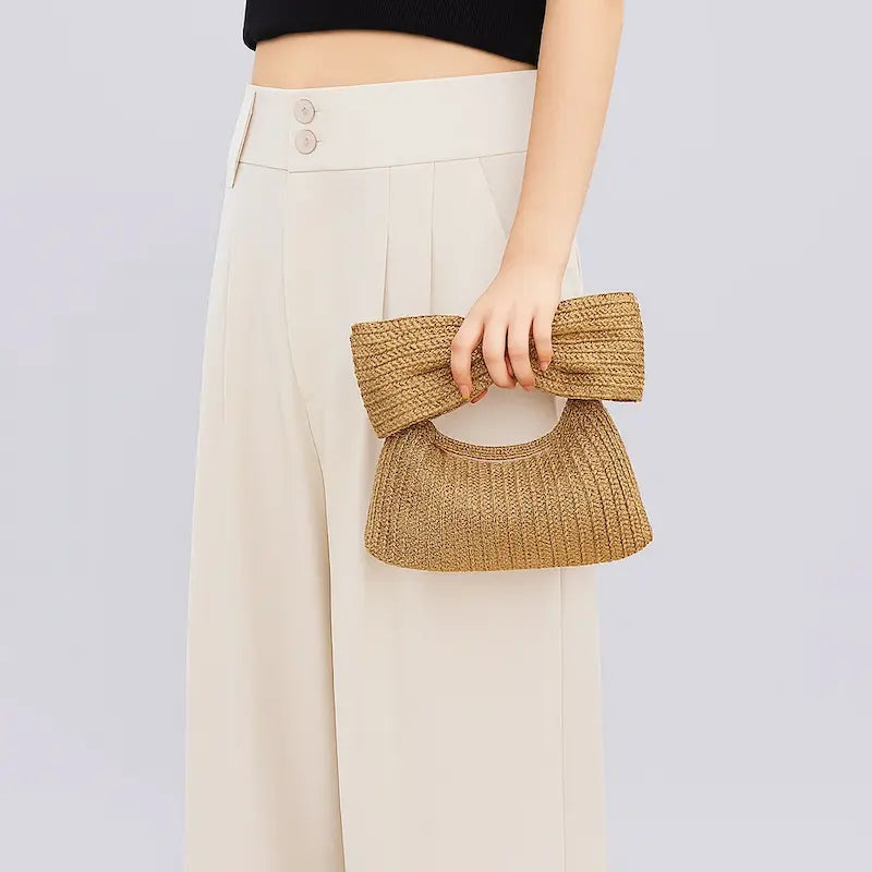 Pochette en paille tressée naturelle avec grand nœud tenue à la main par une femme
