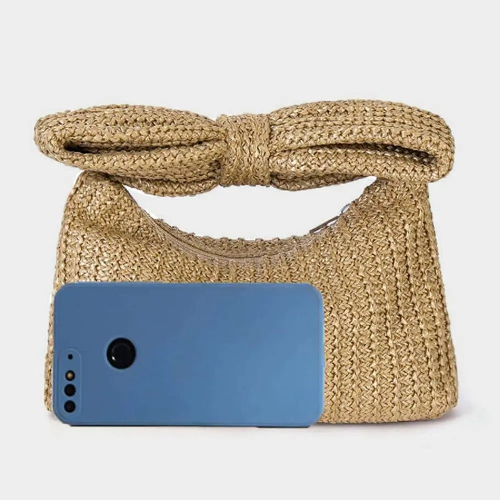 Pochette en paille tressée naturelle avec grand nœud contenant un smartphone