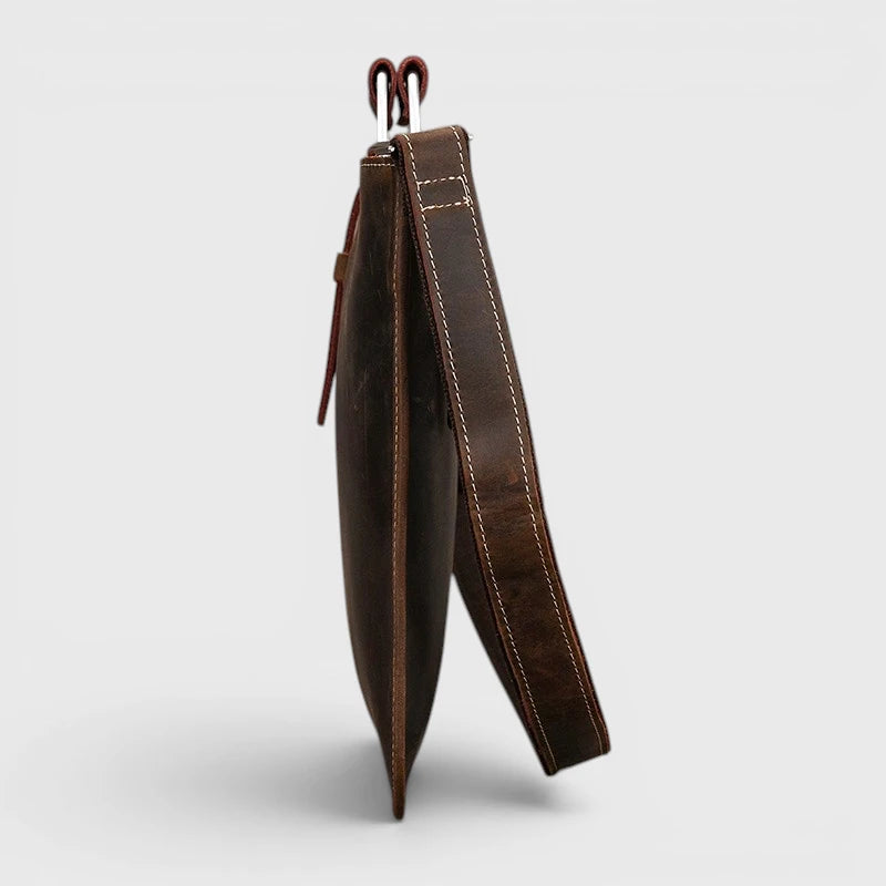 Vue de profil du porte-documents en cuir marron foncé montrant son format fin et sa bandoulière