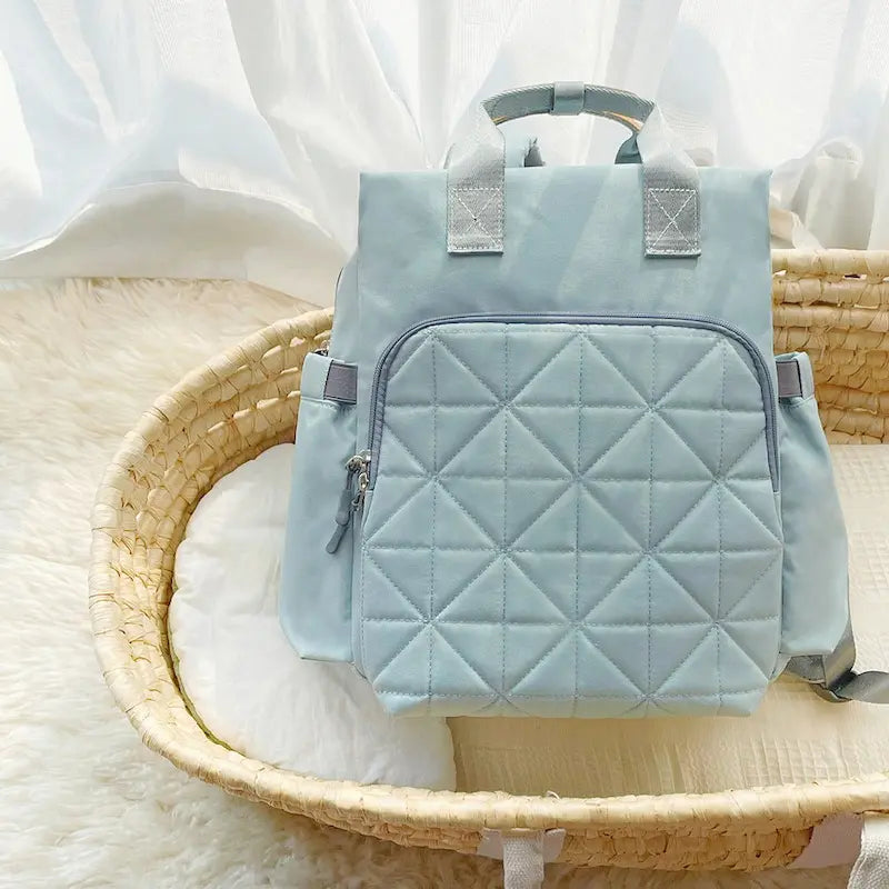 Sac à dos à langer gris clair posé dans un panier en osier