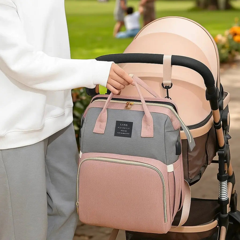 sac à dos à langer lit intégré rose et gris accroché à une poussette