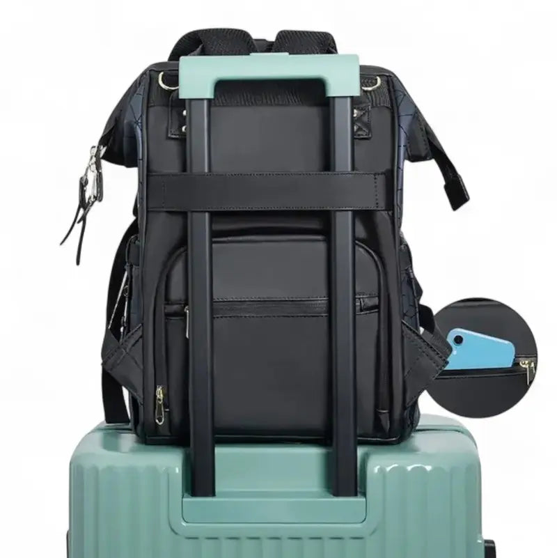 Sac à dos à langer noir fixé sur une valise grâce à une sangle arrière