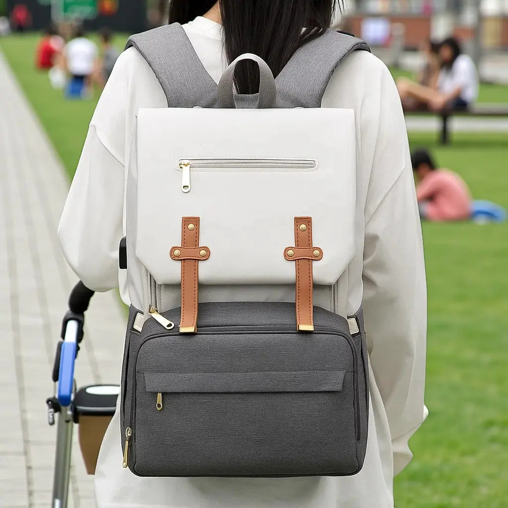 Femme de dos poussant une poussette, portant un sac à dos à langer USB gris et beige sur les épaules