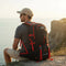 Randonneur assis avec un sac à dos de randonnée 40L noir face à un paysage côtier