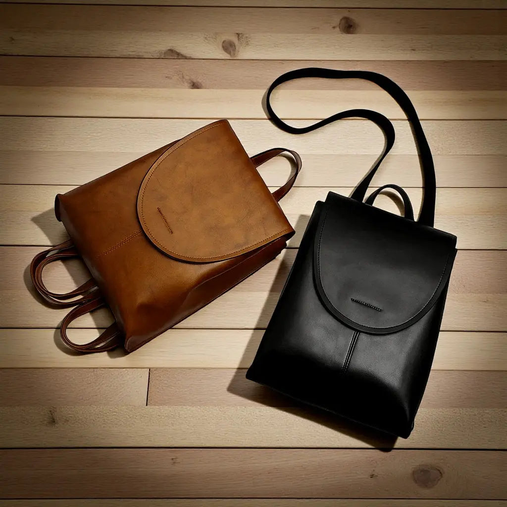 Deux sacs à dos femme en cuir de vachette noir et marron posés a plat sur un plan en bois.