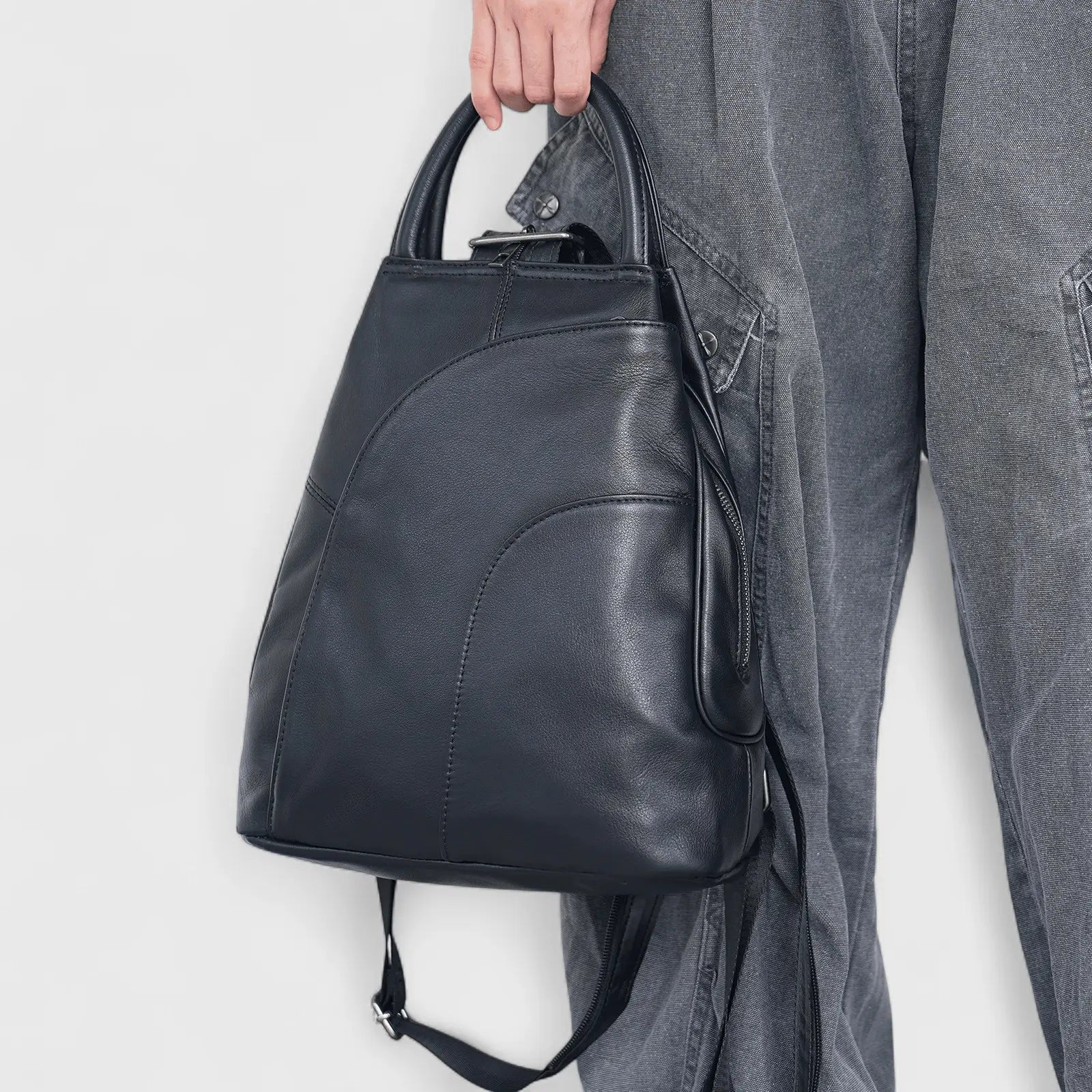 Sac à dos en cuir noir suspendu à une veste grise sur cintre