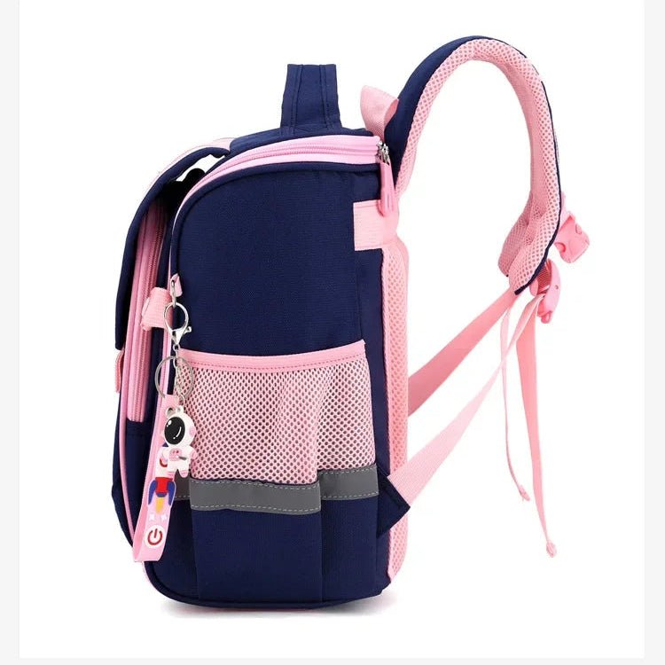 Vue latérale d’un sac à dos fille rose et bleu marine, poche filet rose sur le côté, porte-clés décoratif et bretelles épaissies
