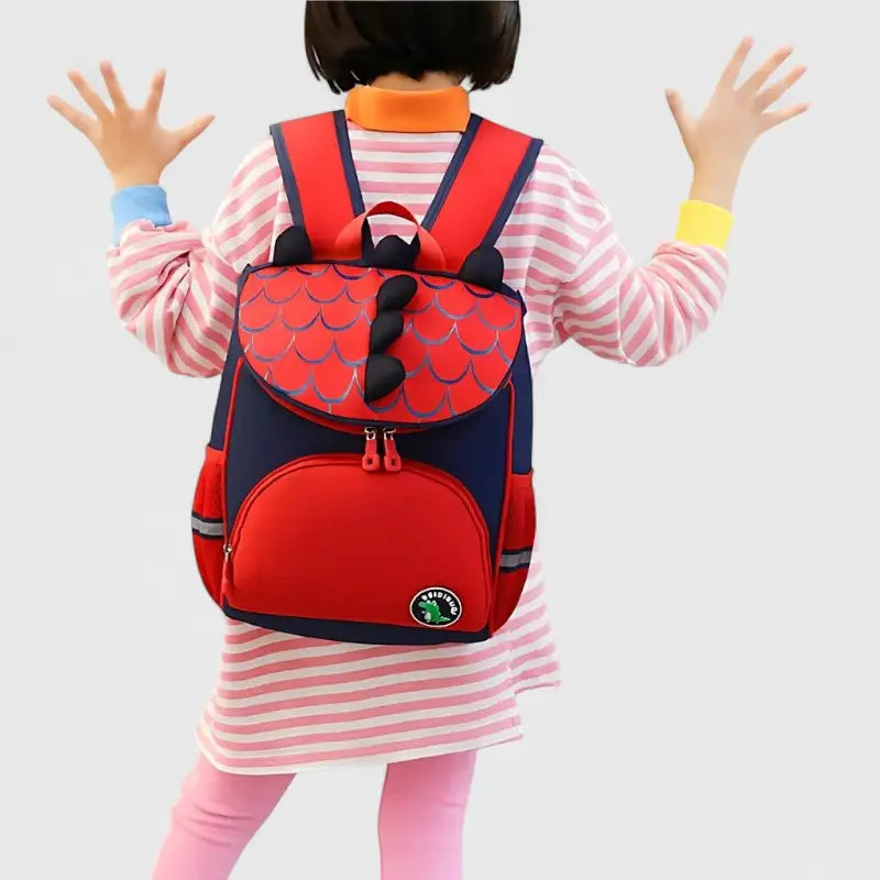 Sac à dos maternelle dinosaure rouge et bleu porté par un enfant.