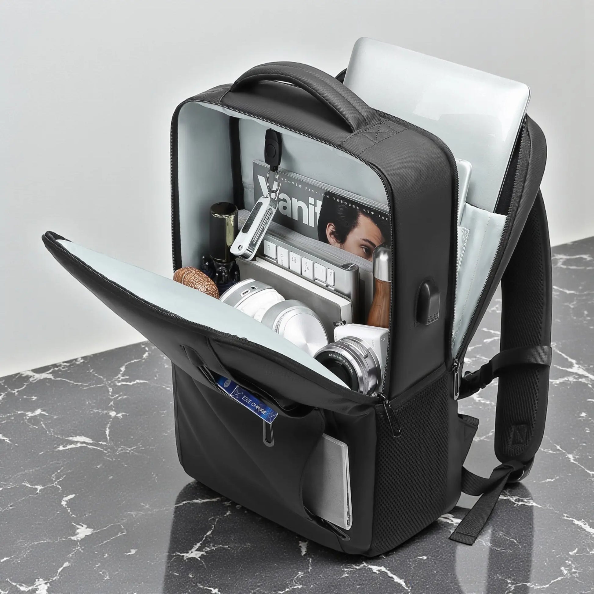 Sac à dos noir pour ordinateur portable ouvert, compartiments internes visibles avec accessoires rangés.