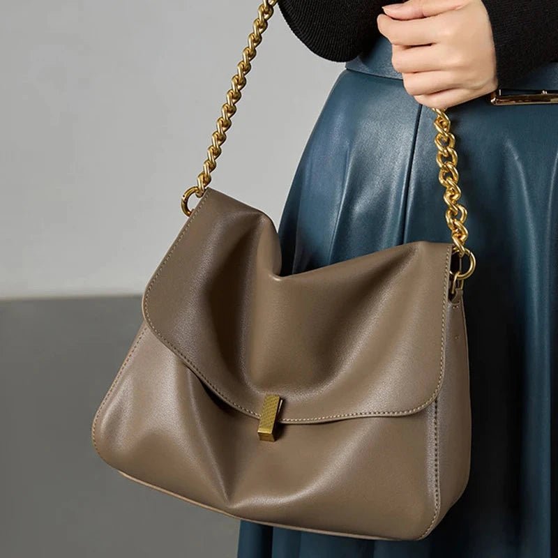 Sac à rabat souple en cuir marron porté à l’avant-bras avec chaîne dorée