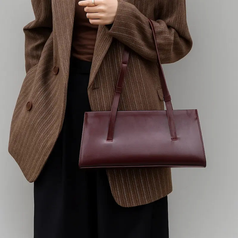 Sac baguette en cuir bordeaux porté par une femme avec manteau marron clair, style chic