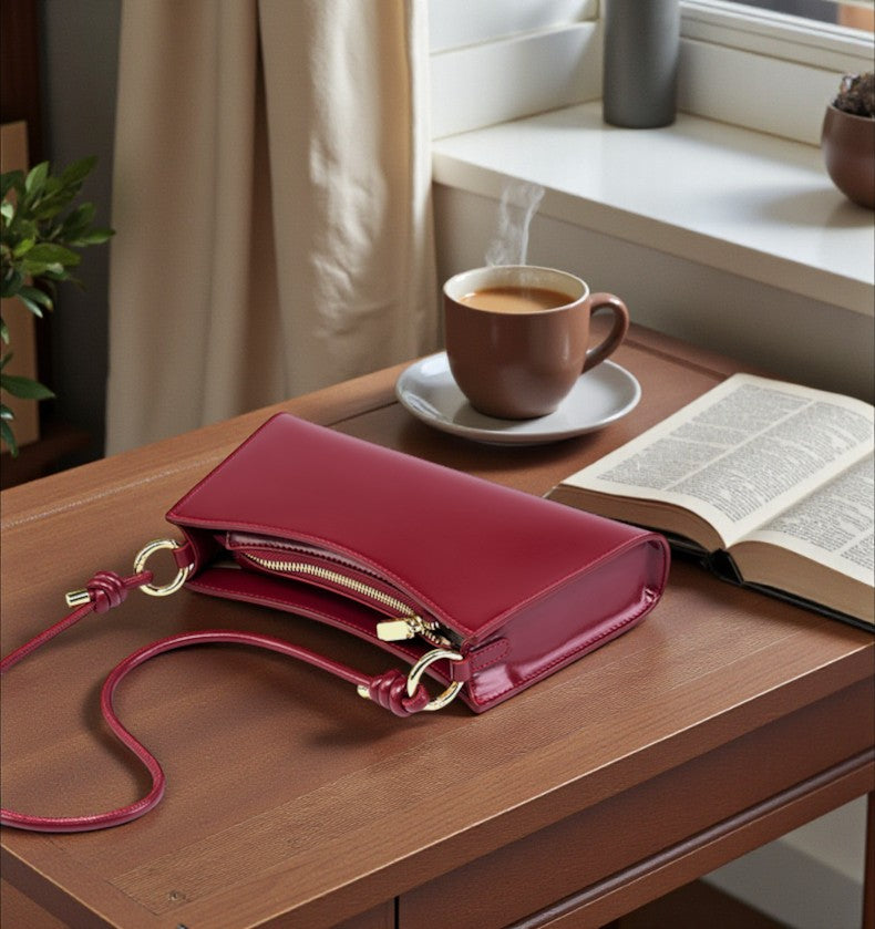 Sac baguette en cuir bordeaux posé sur une table avec accessoires
