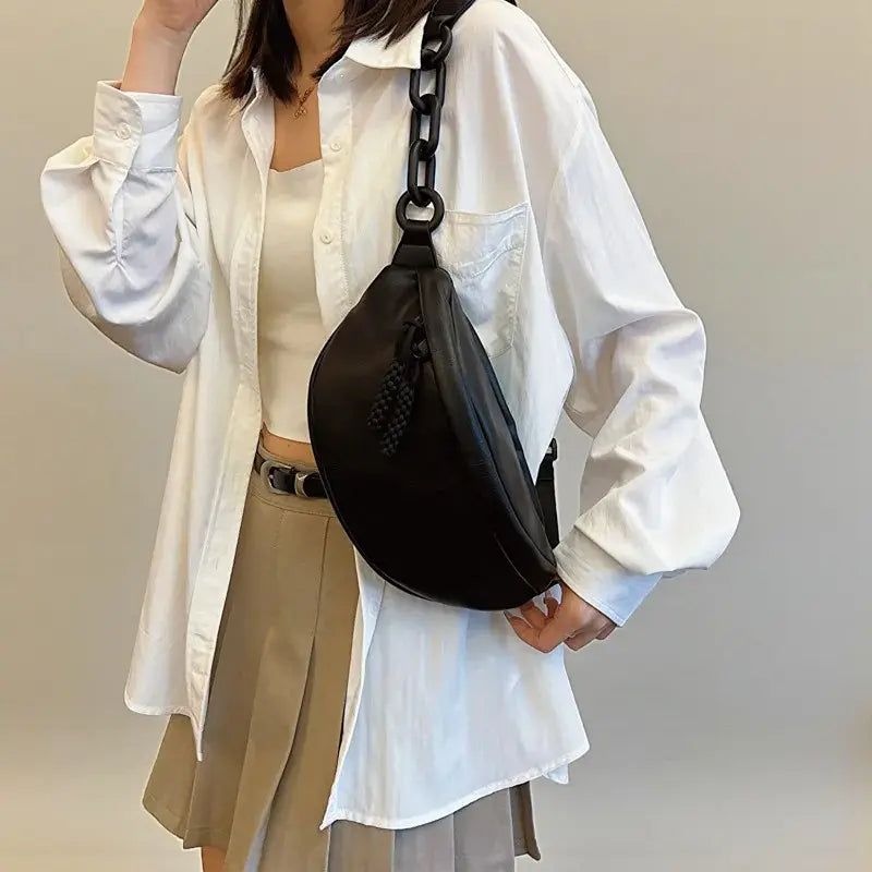 Sac banane femme en cuir synthétique noir porté à l’épaule avec bandoulière réglable.