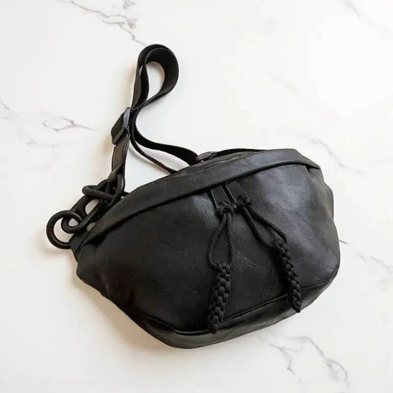 Sac banane femme en cuir synthétique noir posé à plat avec chaîne latérale et bandoulière.
