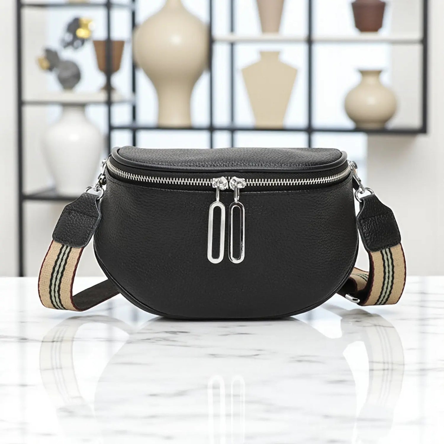 Sac banane femme en cuir véritable noir avec zip double présenté sur une table en exposition.