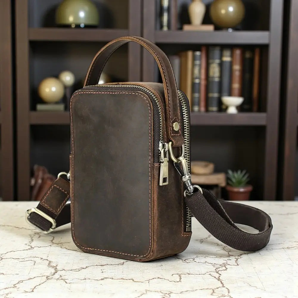 Sac bandoulière compact pour homme en cuir brun vintage – vue de face sur une table en studio.