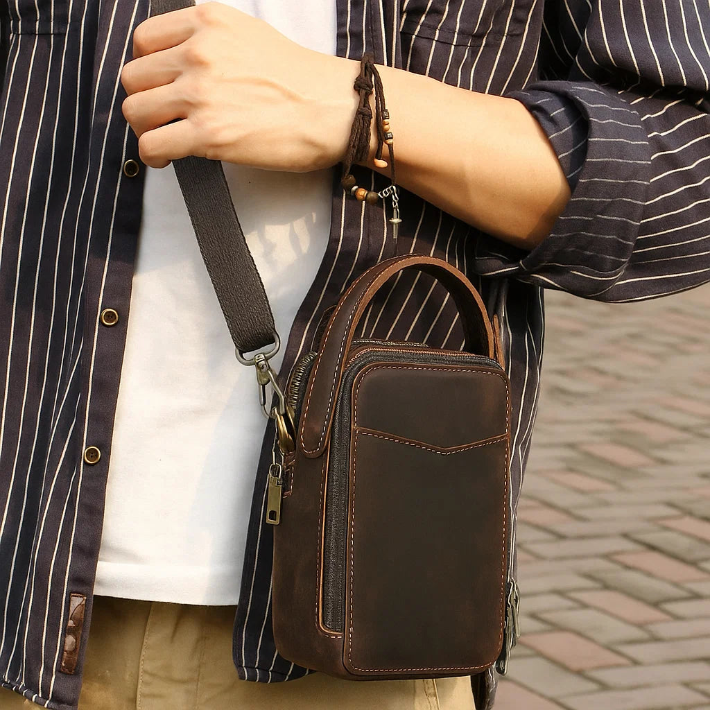 Homme portant un sac bandoulière compact en cuir brun dans un style urbain chic