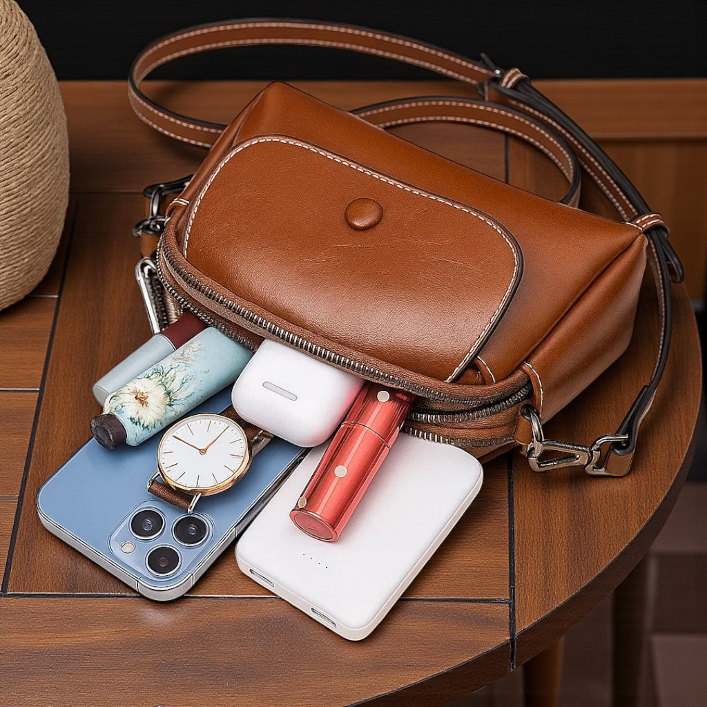 Contenu du sac bandoulière marron foncé avec accessoires du quotidien rangés à l’intérieur.