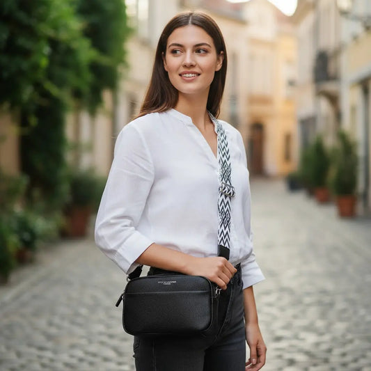 Sac bandoulière noir porté à l'épaule, avec sangle géométrique noire et blanche