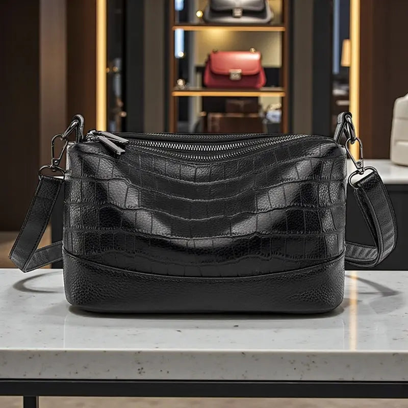 Sac bandoulière en cuir noir façon croco exposé sur table en vitrine
