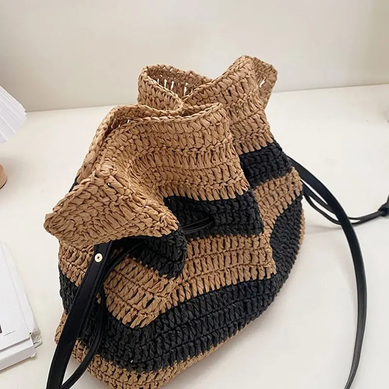 Sac bourse en paille tressée rayé noir et marron vu en angle sur une table