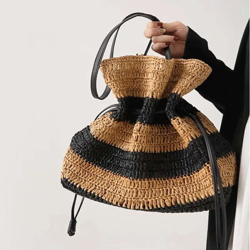 Sac bourse en paille tressée rayé noir et marron porté à la main par une femme