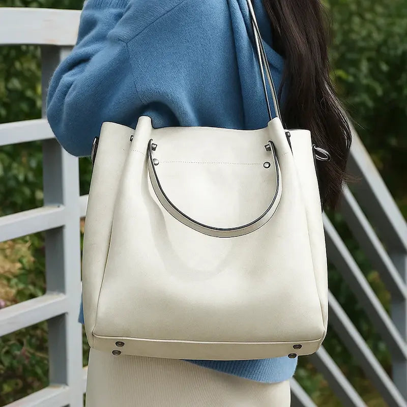 Sac cabas en cuir blanc laiteux porté à l’épaule par une femme en manteau bleu