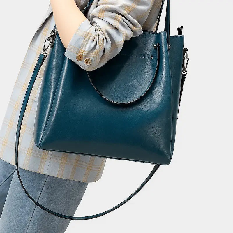 Sac cabas en cuir bleu porté à l’épaule par une femme en manteau gris clair