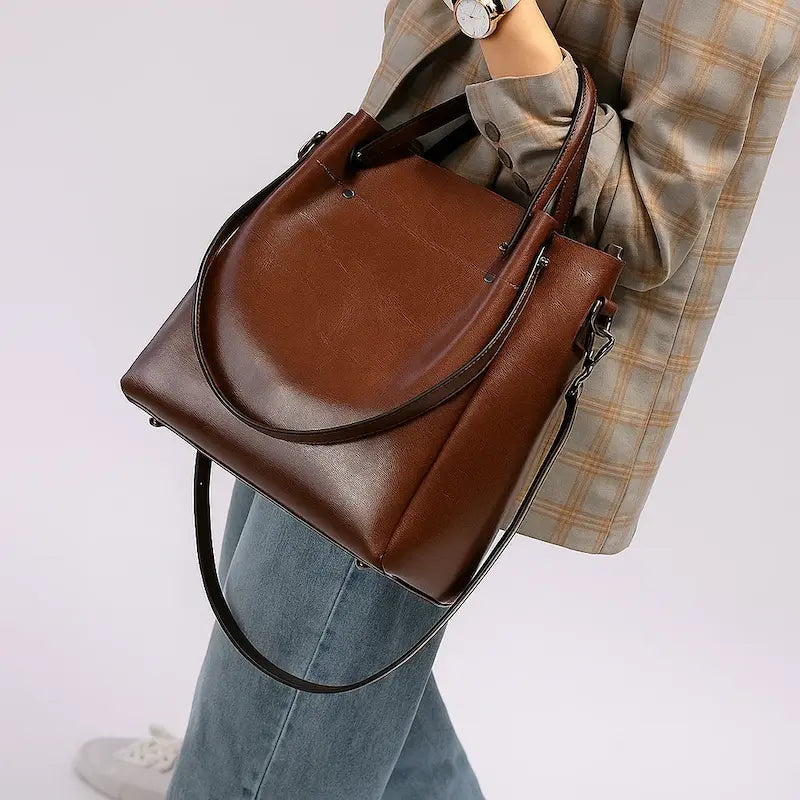 Sac cabas en cuir marron porté à la main par une femme en chemise à carreaux