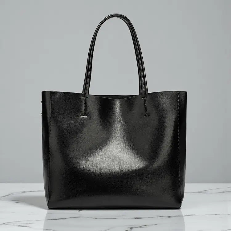 Sac cabas femme en cuir noir brillant posé sur une table en intérieur.