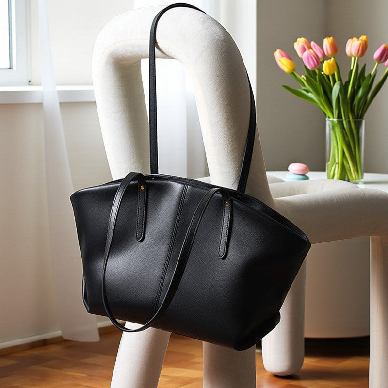 Sac cabas en cuir noir suspendu sur un mannequin près d’une fenêtre, anses longues et structure souple.