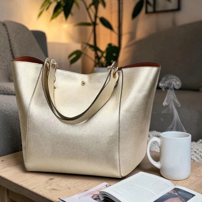 Sac cabas porté épaule métallisé champagne en cuir végétalien posé sur une table de salon avec tasse et livre
