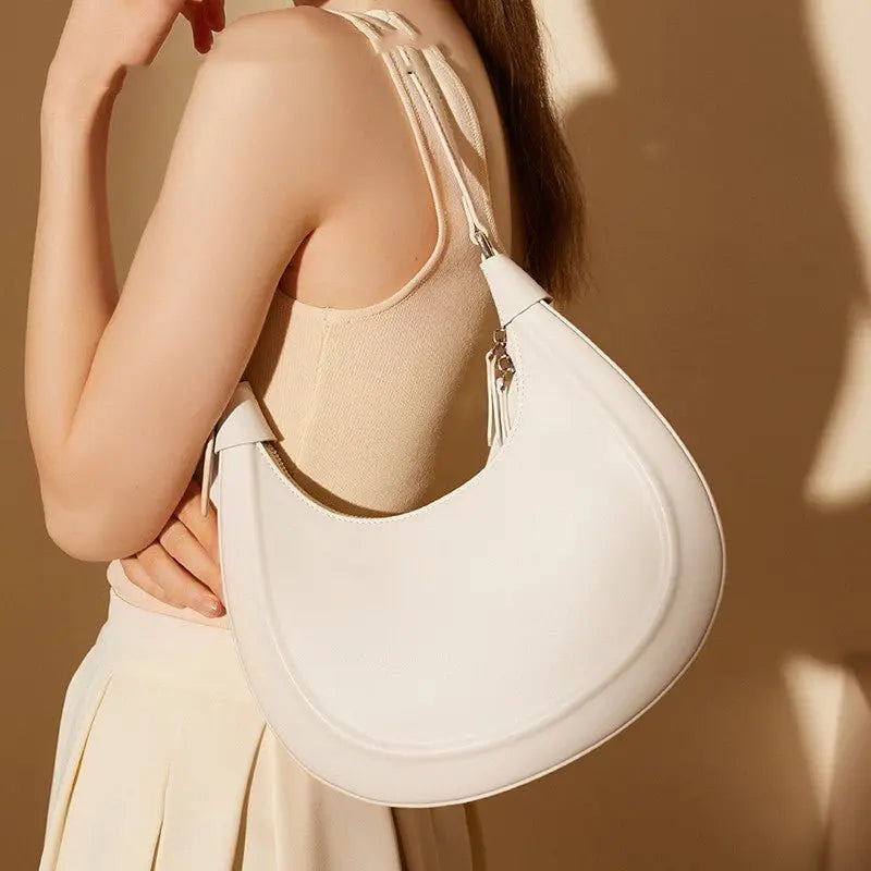 Sac croissant en cuir véritable blanc porté à l’épaule par une femme en robe beige