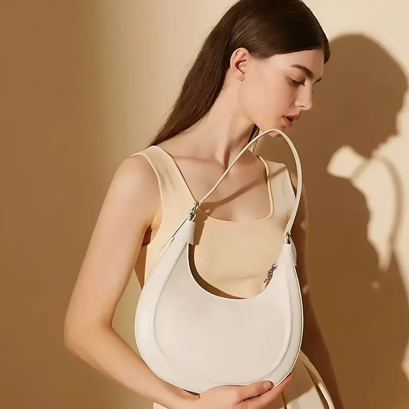 Sac croissant en cuir véritable blanc porté à l’épaule par une femme en robe beige