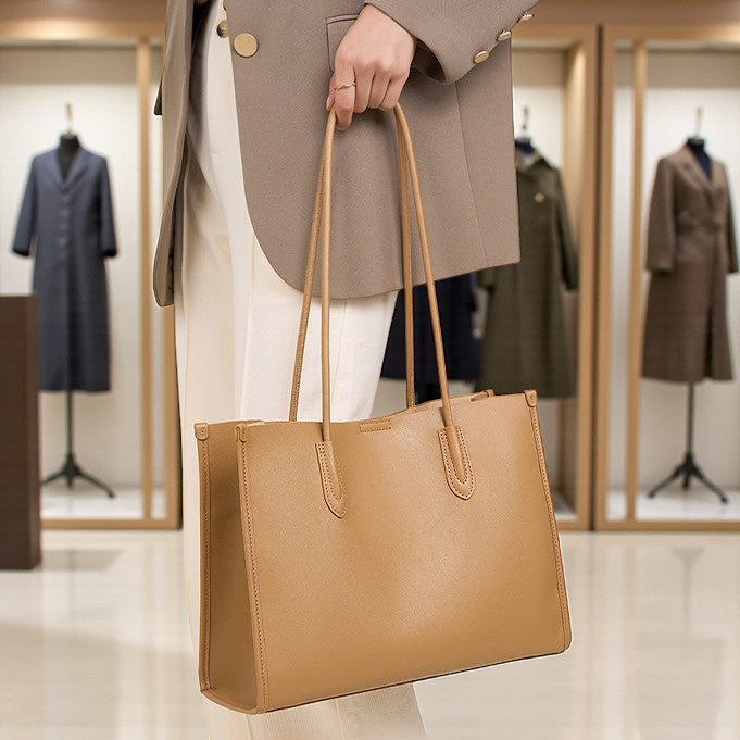 Sac en cuir camel porté à la main par une femme dans une boutique, longues poignées visibles