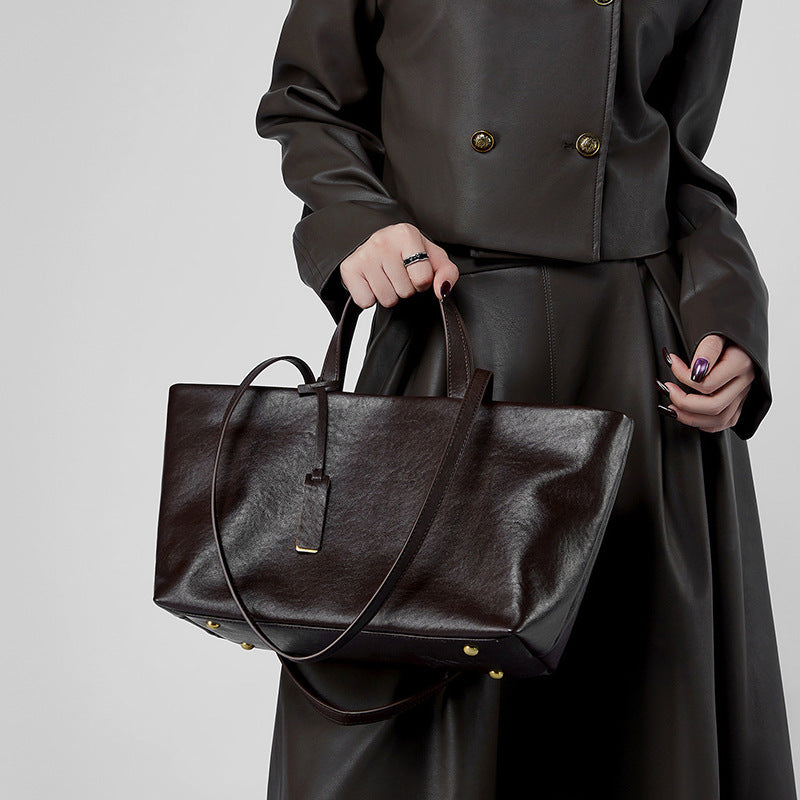 Sac en cuir marron foncé porté à la main par une femme en extérieur, style rétro élégant