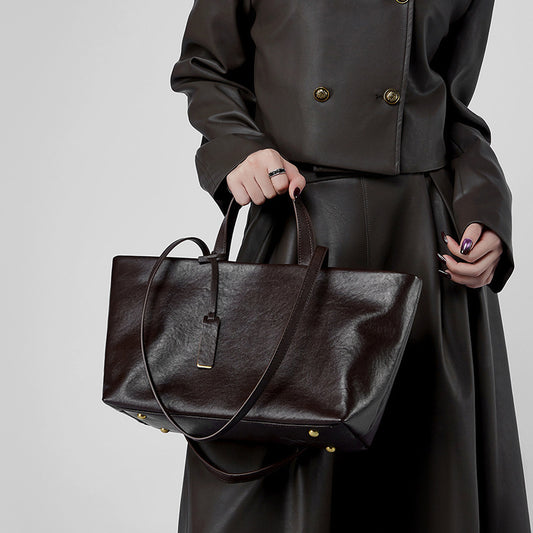 Sac en cuir marron foncé porté à la main par une femme en extérieur, style rétro élégant