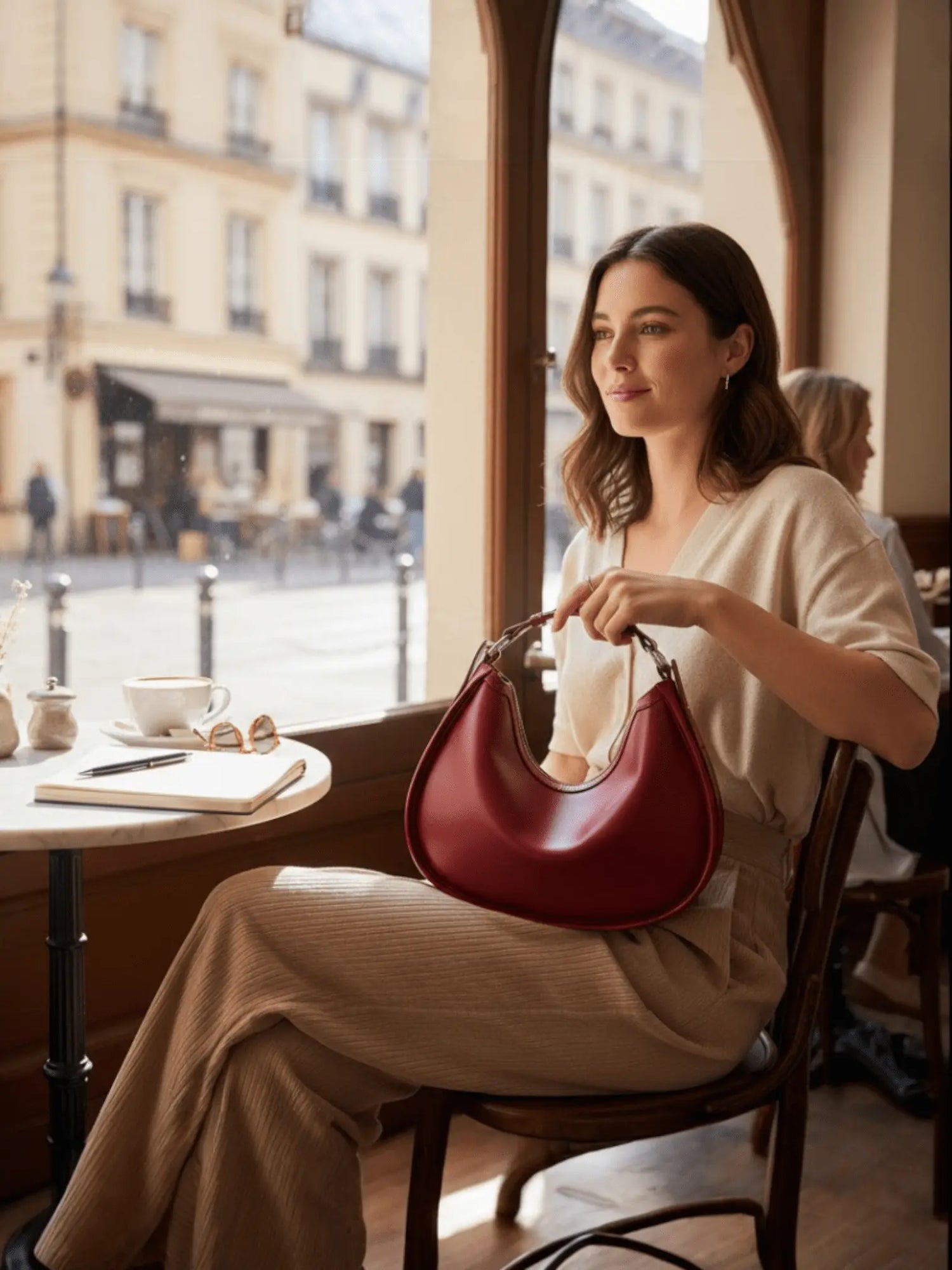 Femme assise dans un café  avec un sac en cuir rouge de forme croissant tenu à la main.
