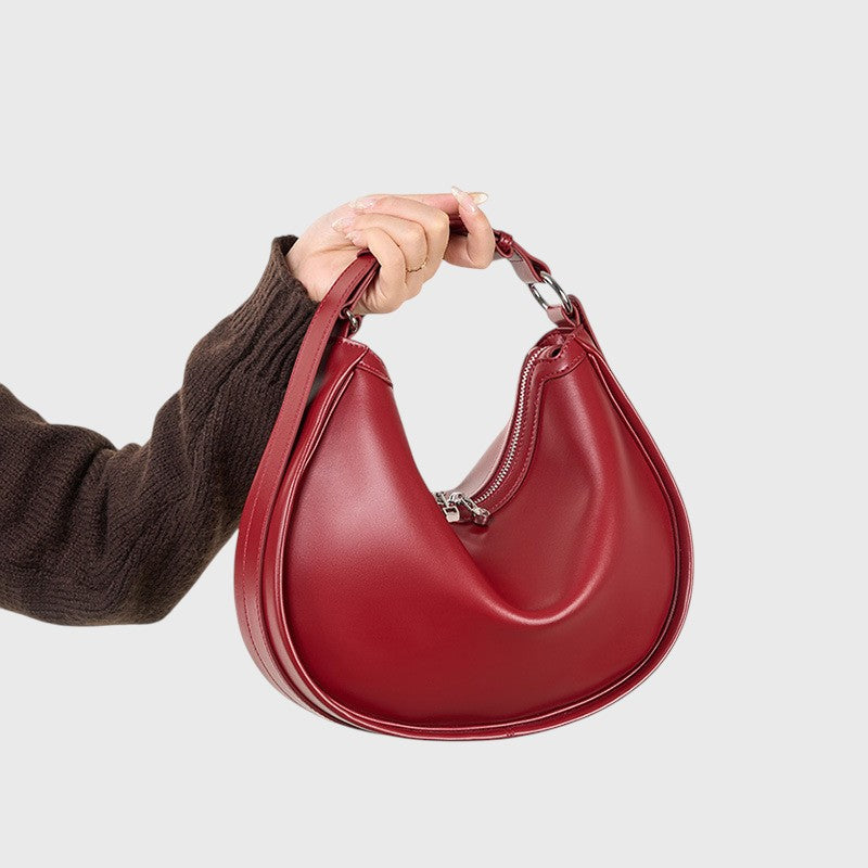 Vue de face d’un sac en cuir rouge de forme croissant avec fermeture zippée.