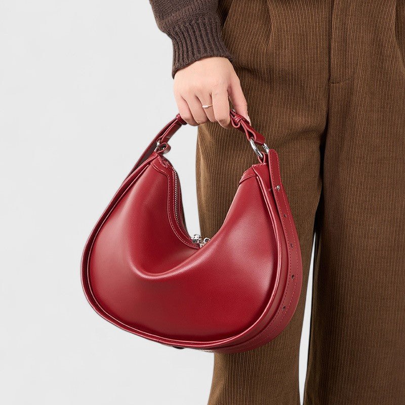 Femme tenant un sac en cuir rouge de forme croissant par la poignée courte.