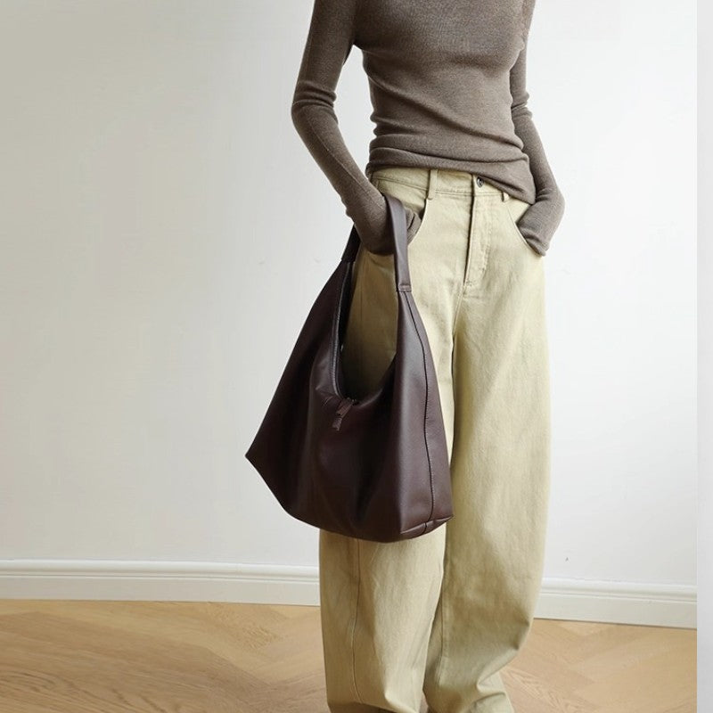 Sac marron en cuir de vachette porté à l’épaule, vue en pied dans une tenue beige.