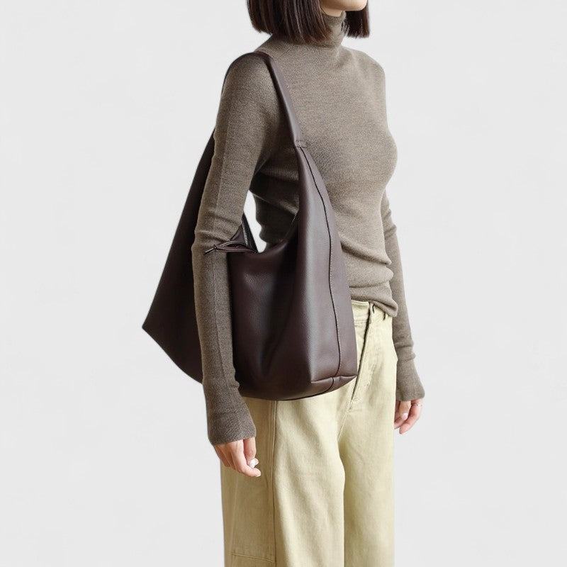 Vue latérale du sac épaule marron en cuir de vachette porté avec un pull beige.