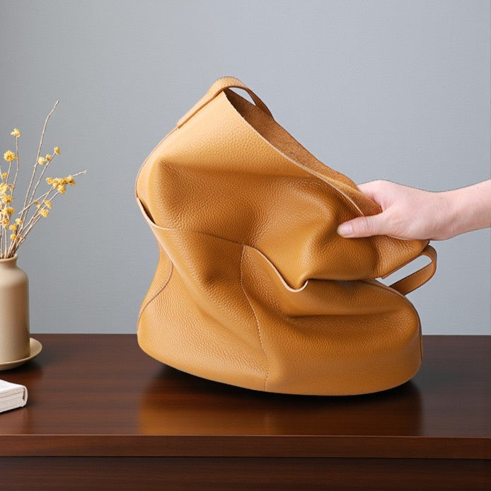 Main tenant un sac fourre-tout camel en cuir souple posé sur une table