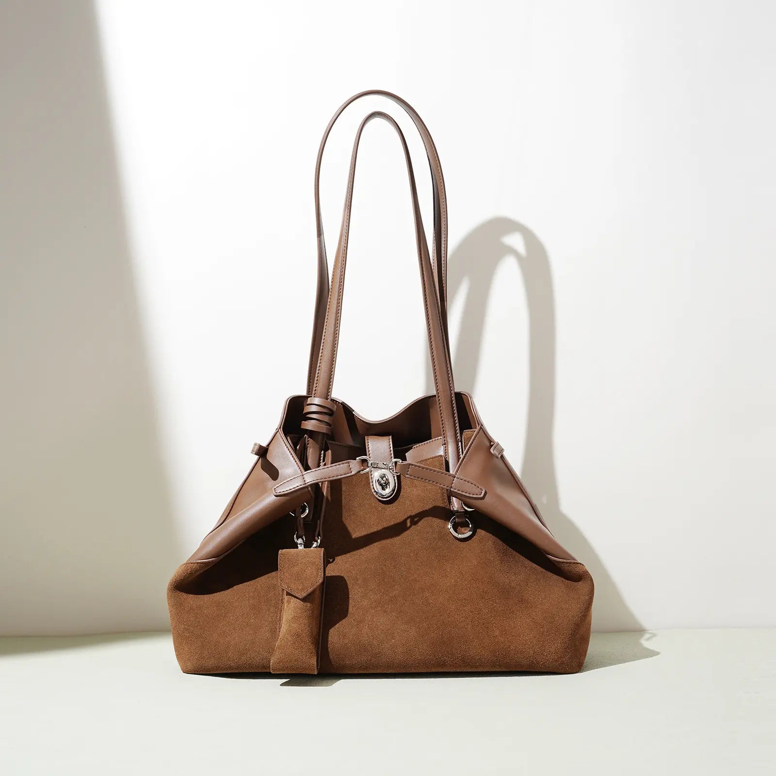 Sac à main en cuir marron avec double anses longues, ombre portée sur fond clair