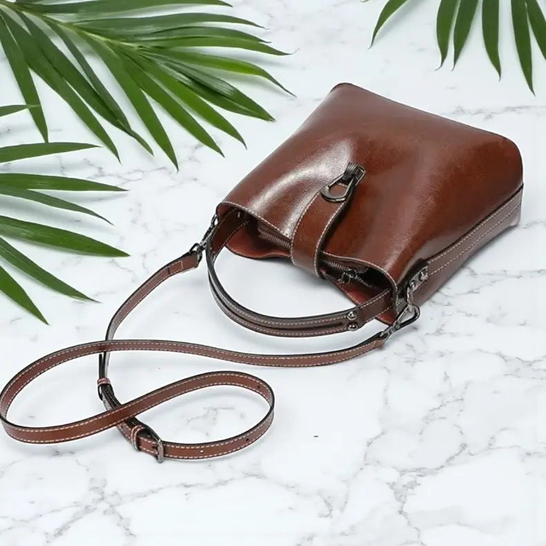 Sac à main vintage en cuir marron avec bandoulière réglable, posé à plat sur fond marbré.