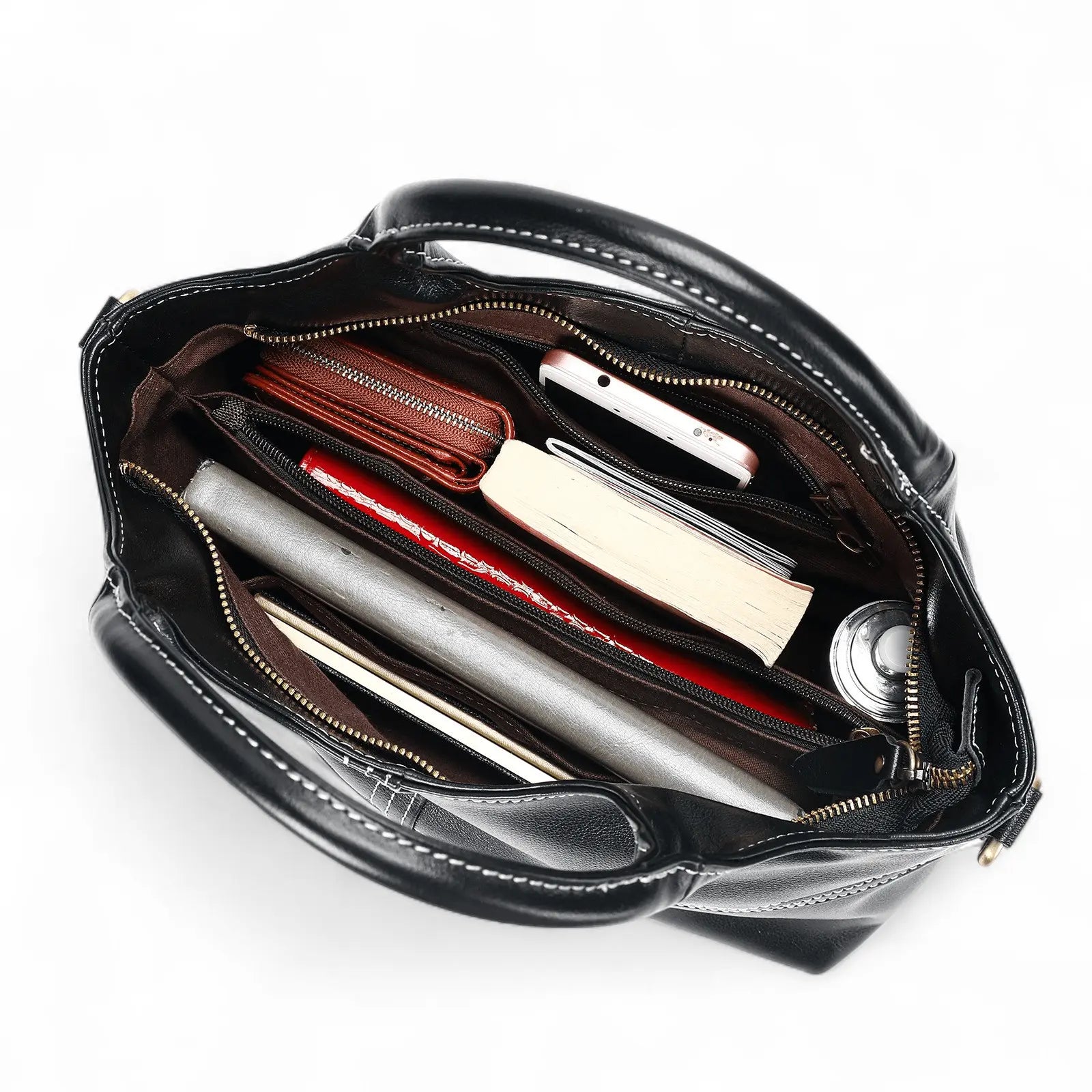 Intérieur du sac à main en cuir noir contenant des livres, trousse et portefeuille.