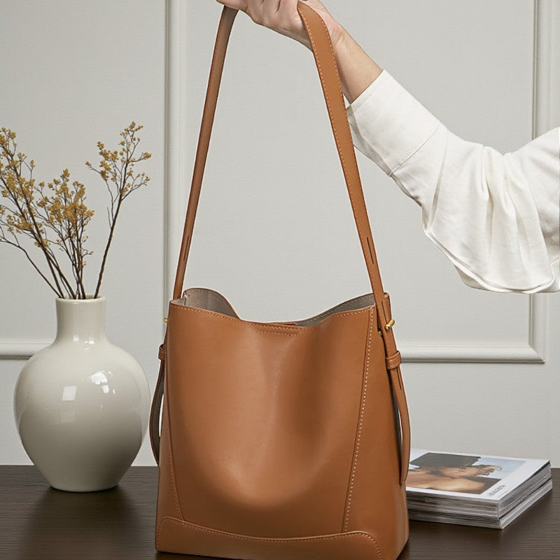 Vue de face d’un sac messager en cuir camel posé sur une table, bandoulière tombante.